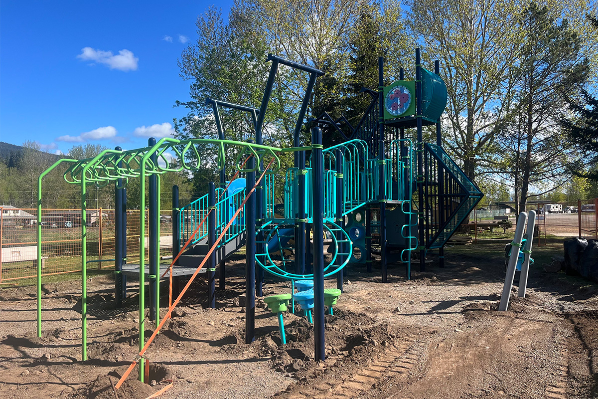Teal and green play tower under construction on a bare dirt site, a finishing step in how to design a commercial playground.