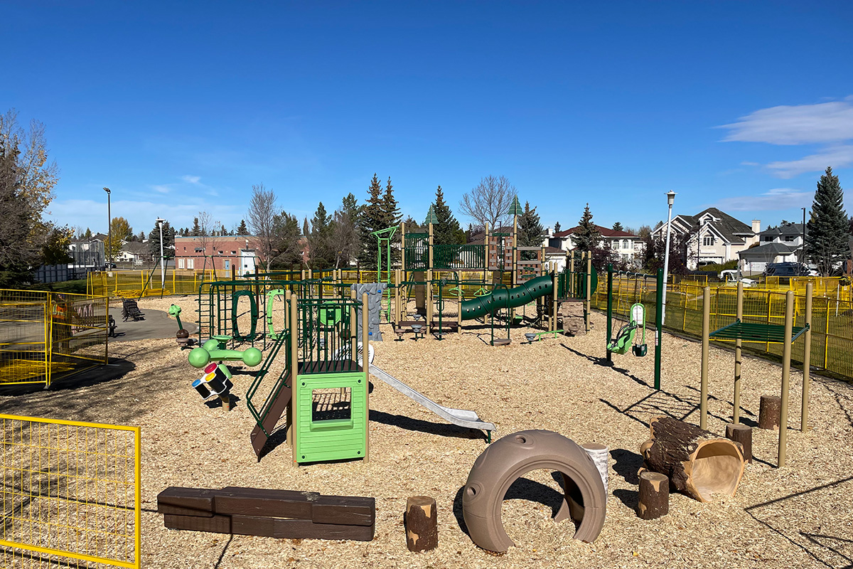 Wide view of a playground with yellow safety fencing, log and tire climbers, showing how to design a commercial playground.