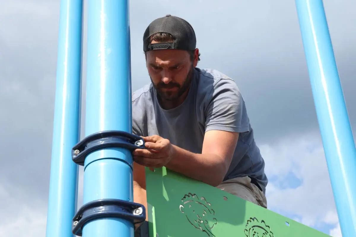 Once school playground planning wraps up, an installer fastens a clamp to a blue post.