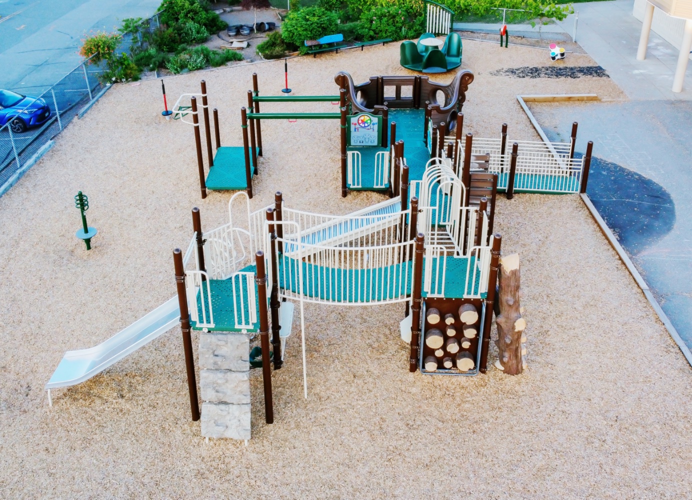 Aerial view of a brown and green structure with an ship rocker and metal slide on wood chips beside the school.