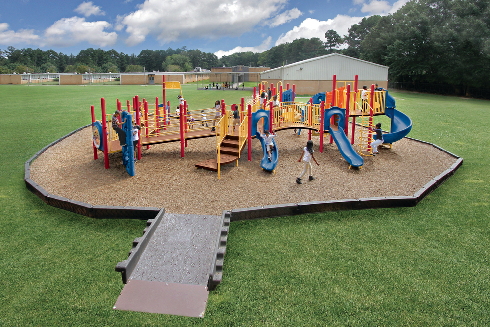 Ramp leads onto wood mulch, one of several playground surfacing options, around a red, yellow and blue structure.