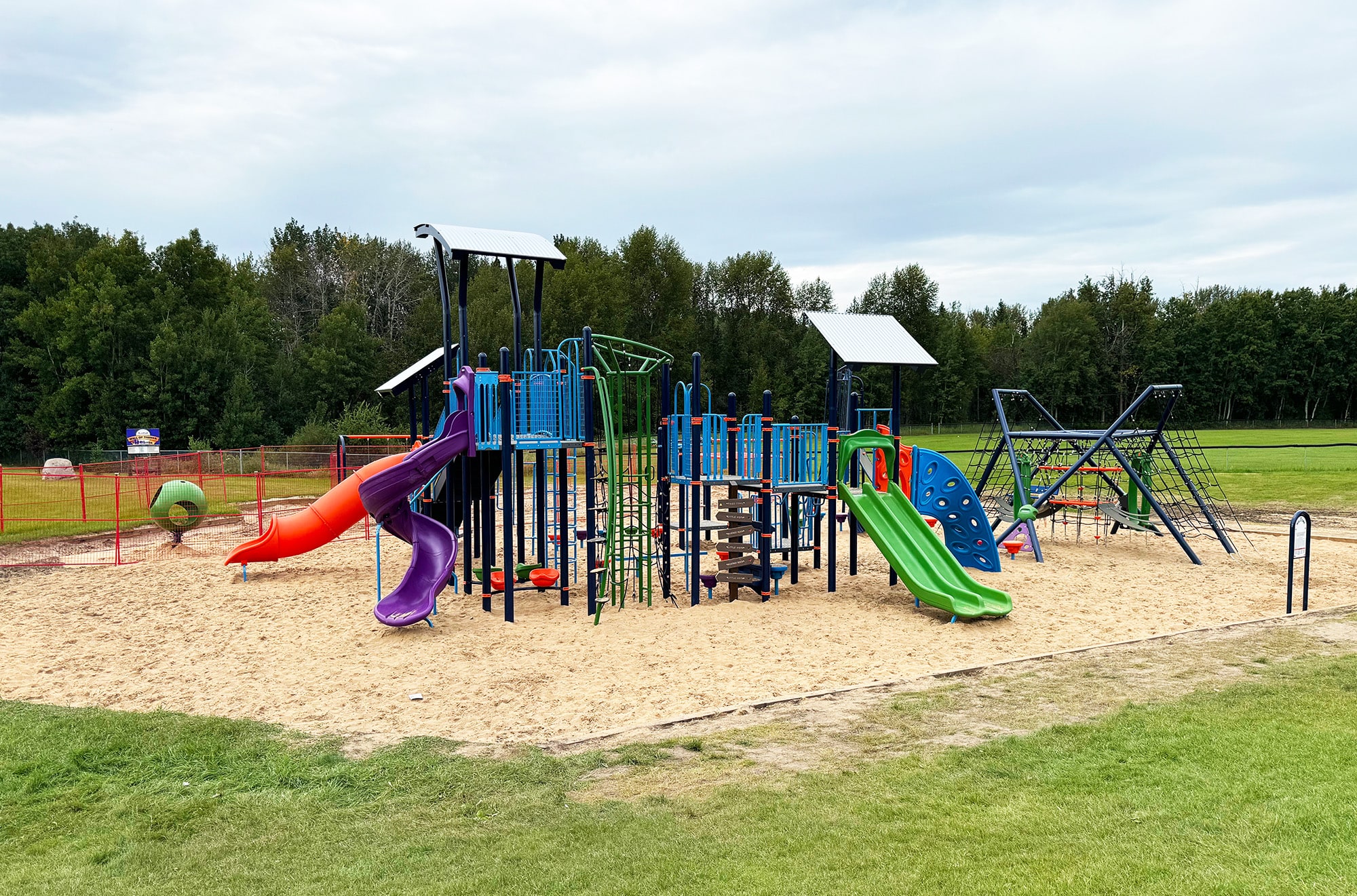 Navy play structure with orange and purple spiral slides, a green slide and rope climber on sand.