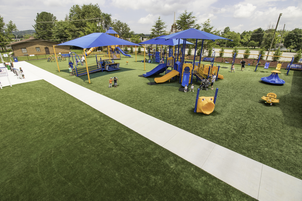 Artificial turf, one of many playground surfacing options, covers this play area under blue shade sails.