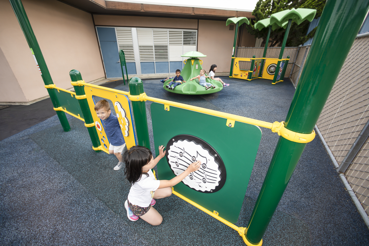 Child at a music panel in a courtyard with a spinner, featuring playground equipment for small spaces.