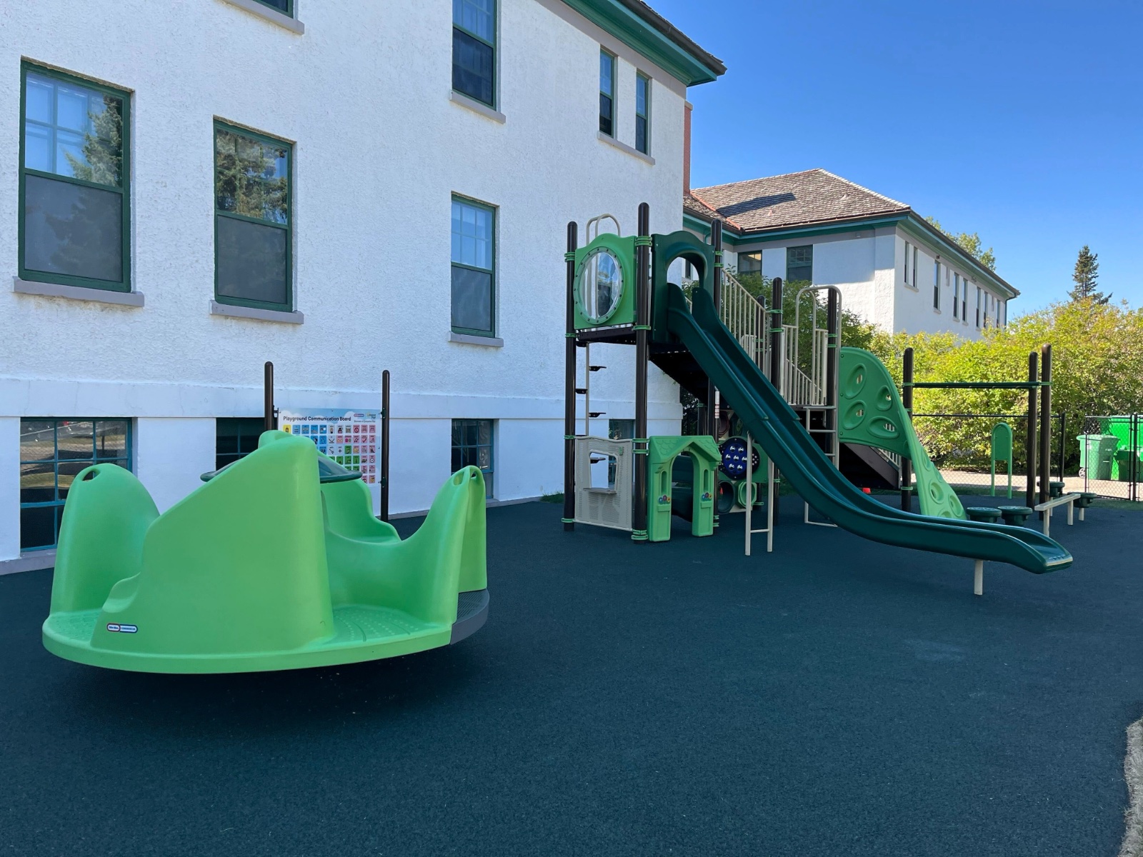 A merry-go-round and compact slide structure show how playground equipment for small spaces fits beside a building,