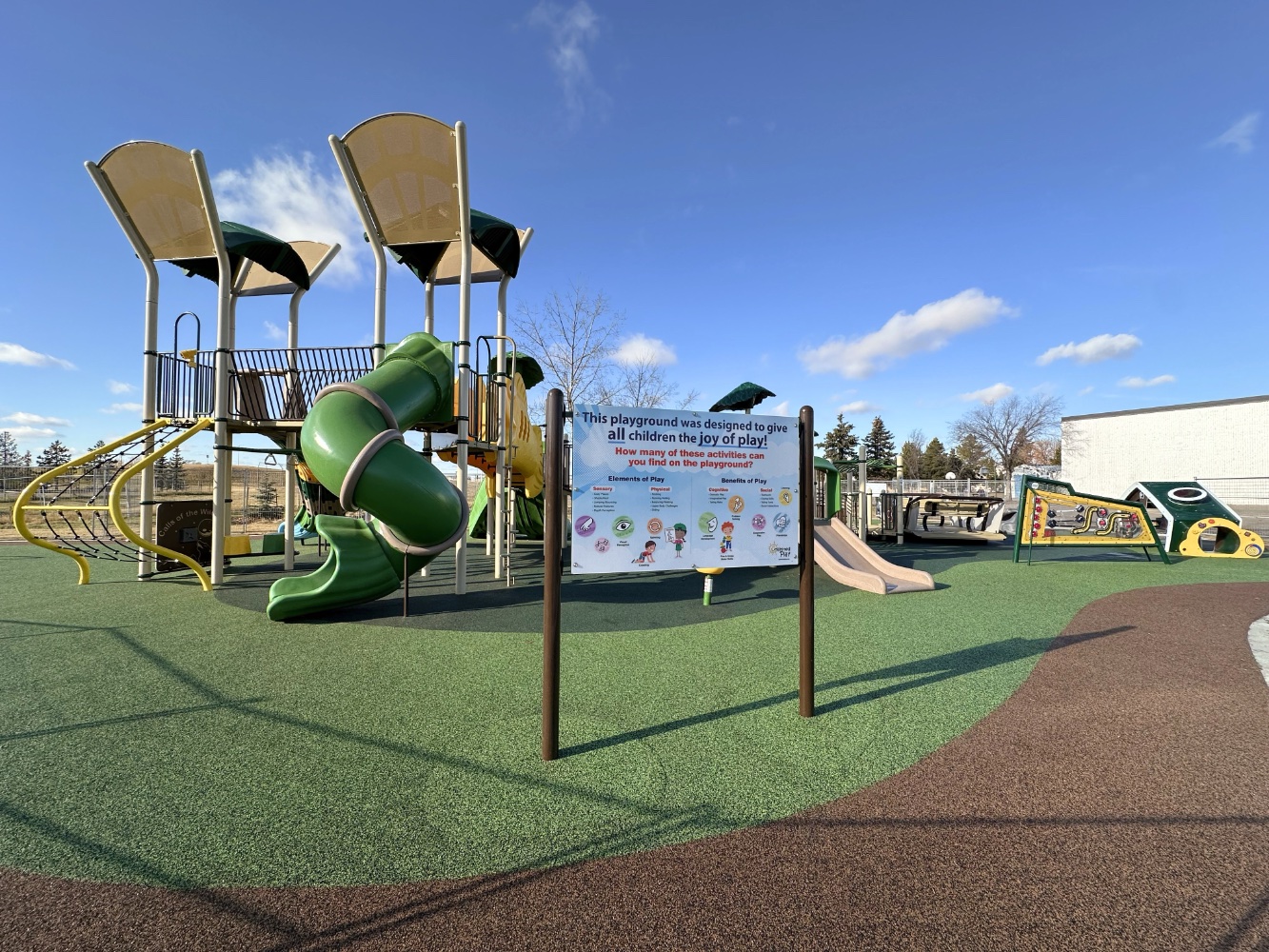 Sign with tips on inclusive play in front of a green tube slide, sensory panel and tan slide on rubber surfacing.