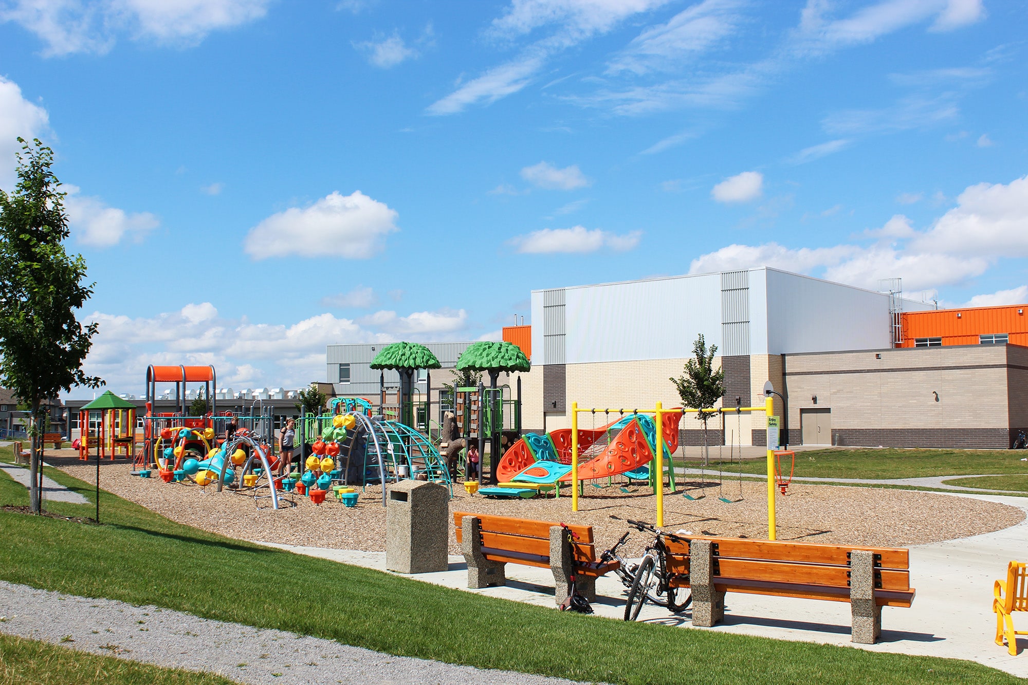 Benches and a walking path frame a colourful play area, where school playground planning grouped climbers and swings.