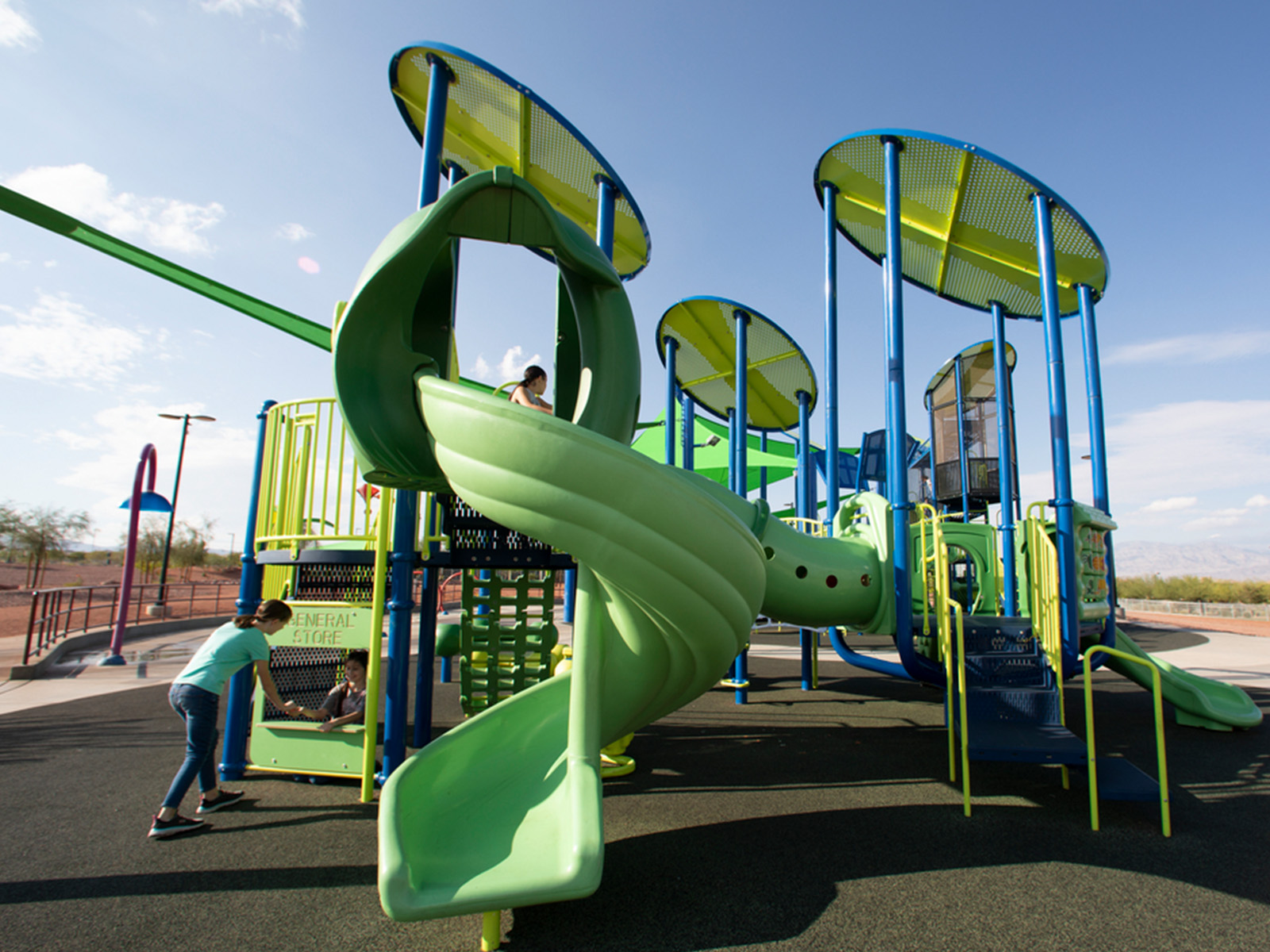Lime and blue play structure with a spiral slide and round shade canopies, kids at a store panel.